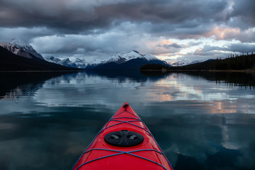 Kayaking in a peaceful and calm glacier lake during a vibrant cloudy sunset. Taken in Maligne Lake,...