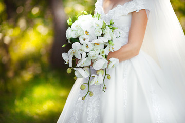 the bride holds a large bouquet and white orchids and white roses.