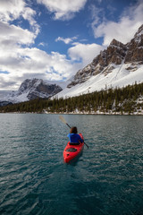 Adventurous girl kayaking in a glacier lake surrounded by the Canadian Rockies during a cloudy morning. Taken at Bow Lake, Banff, Alberta, Canada.