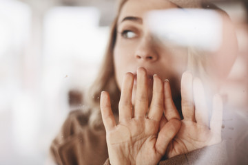 Amazed beautiful female look under the glass window, cover mouth. Woman wears total look. Beige beret. Hand on glass. Focus on hand