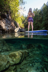 Over and Under Picture of a young Caucasian girl paddle boarding in a river during a sunny summer day. Taken in Alouette Lake, near Vancouver, BC, Canada.