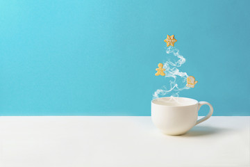 Cup of tea or coffee with steam in fir tree shape with gingerbread cookies on blue background. Christmas celebration concept. Copy space. Toned