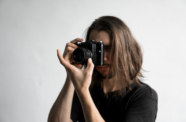 Handsome young bearded man with a long hair and in a black shirt holding vintage old-fashioned film...