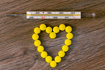 Tablet pills in blister packs and white thermometer on wood background. Pharmacy, medicine and...