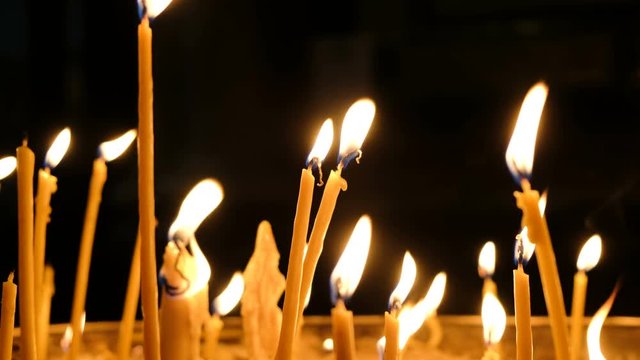 Wax candles burn in the dark in church against dark background