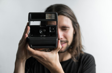 Handsome young bearded man with a long hair and in a black shirt holding vintage old-fashioned film...