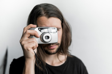Handsome young bearded man with a long hair and in a black shirt holding vintage old-fashioned film...