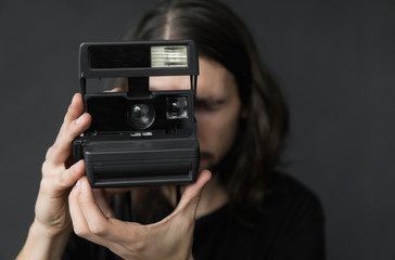 Handsome young bearded man with a long hair and in a black shirt holding vintage old-fashioned film...
