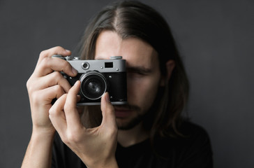 Handsome young bearded man with a long hair and in a black shirt holding vintage old-fashioned film...