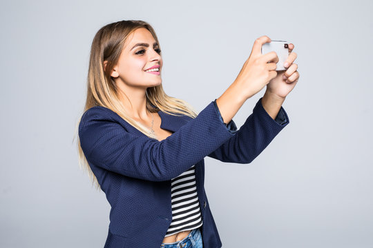 Young woman takes photographs with her mobile phone isolated on white background