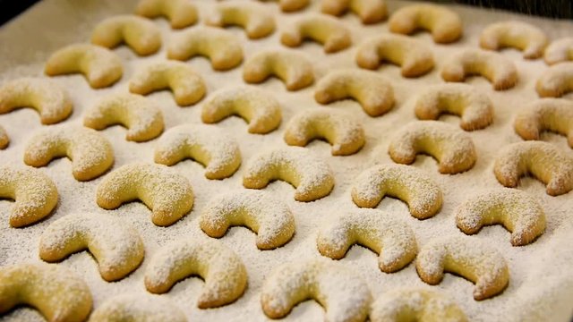 Footage of process of powdering with icing sugar home baked German and Austrian traditional Christmas cookies vanilla crescents on white parchment paper on tray. Holiday baking concept