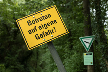 Gelbes Warnschild Betreten auf eigene Gefahr vor unscharfem Wald