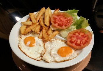 Plato combinado con dos huevos fritos, ensalada y patatas fritas.