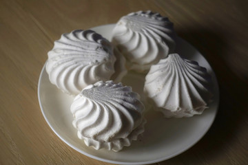 Marshmallow four delicious sweet desserts of white marshmallows zephyr on a plate in contrast lighting on a wooden table. Lack of coverage. Evening