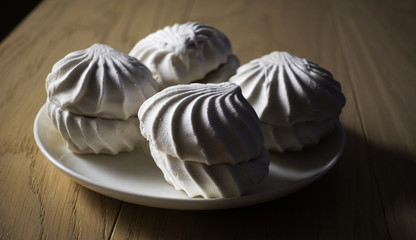 Marshmallow four delicious sweet desserts of white marshmallows zephyr on a plate in contrast lighting on a wooden table. Lack of coverage. Evening