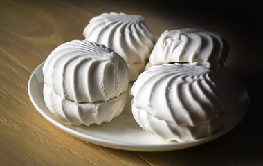 Marshmallow four delicious sweet desserts of white marshmallows zephyr on a plate in contrast lighting on a wooden table. Lack of coverage. Evening