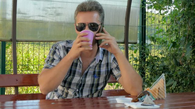 man in glasses in the gazebo talking on the phone, eating a coffee sandwich