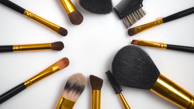 Makeup brushes set rotated over white background. Various professional makeup brushes. Make up artist tools. Flatlay, top view. 4K UHD video footage. 3840X2160