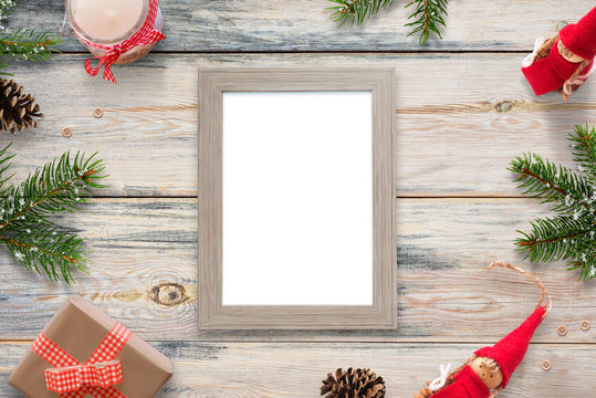 Isolated picture frame surrounded with Christmas decorations, fir branches, dolls, gifts and candles.