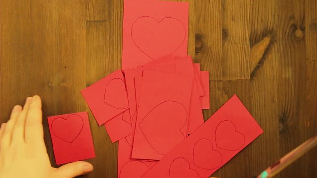The girl cuts from the red cardboard blank with hearts. Time laps