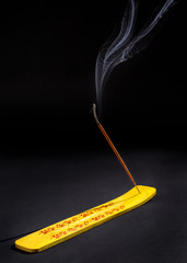 Burning incense stick in yellow holder on the dark background with smoke floating above