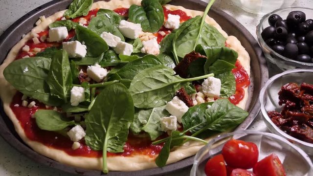 Preparing pizza toping. Laying fresh spinache leaves on pizza topping.