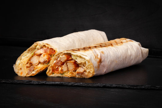 Shawarma sandwich gyro- fresh roll of thin lavash (pita bread) filled with grilled meat, mushrooms, cheese, cabbage, carrots, sauce, green. Traditional Eastern snack. On dark black background