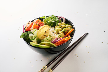 poke bowl with salmon, avocado, cucumber, arugula, broccoli, rice, carrot and sweet onions with chopsticks isolated over white background. side view