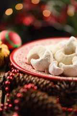 Traditional Austrian Christmas pastry: vanilla crescent vanillekipferl. Homemade nut cookies in icing sugar on red plate decorated with fir cones