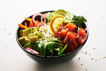 poke bowl with salmon, avocado, cucumber, arugula, broccoli, rice, carrot and sweet onions isolated over white background. side view