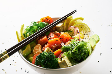 poke bowl with salmon, avocado, cucumber, arugula, broccoli, rice, carrot and sweet onions with chuka salad, chopsticks isolated over white background. side view close-up