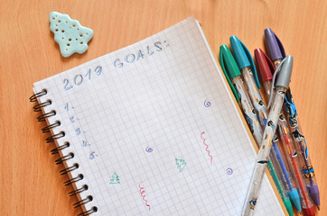 2019 New year's goals on a notebook on a wooden table with a blue Christmas tree and pens