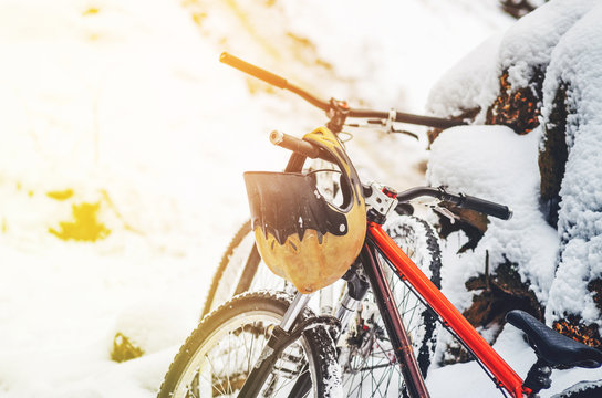 Full face helmet hangs on the bicycle handlebars in snowy winter forest. Mountain bike safety concept. Extreme sport background