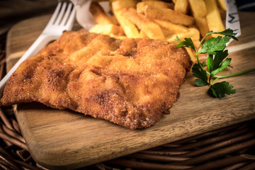 A piece of fried cod with fries on cutting board.