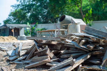 Closeup pile of useless wood at the construction site with blurred concrete mixer in background