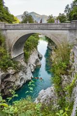 Fototapeta na wymiar The Napoleon bridge near Kobarid in Slovenia. People are kajaking in the beautiful turquoise colored water of the Soca river