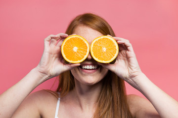 Funny young woman posing with orange slices over pink background.