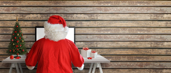 Santa Claus send greeting cards online. Copy space beside on wooden wall.
