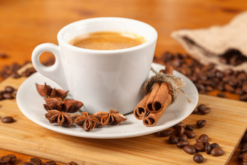 White espresso Cup on the background of coffee beans, cinnamon, anise. Fresh dark black strong Americano coffee on wooden table, thick foam in coffee, morning refreshing hot drink caffeine, close-up