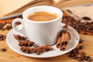 Coffee break a Cup of hot coffee and a book on a wooden table. A white Cup of black coffee surrounded by a small amount of roasted coffee beans, cinnamon, anise and an open book