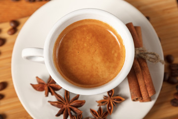 White espresso Cup on the background of coffee beans, cinnamon, anise. Fresh dark black strong Americano coffee on wooden table, thick foam in coffee, morning refreshing hot drink caffeine, top view
