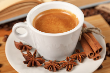 Coffee break a Cup of hot coffee and a book on a wooden table. A white Cup of black coffee surrounded by a small amount of roasted coffee beans, cinnamon, anise and an open book