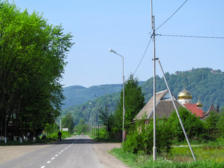 Summer landscape of Ivan Chendey street in Khust with the ruins of an ancient fortress on a hill....