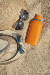 Male and female sunglasses,  sunhats and a sunprotection cream at the sand as a reminder of protection importance during the sun exposure.