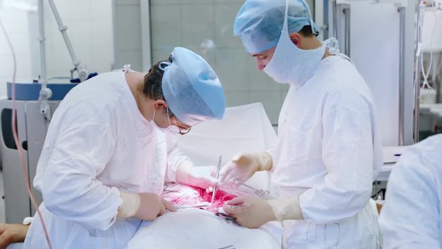 Two male surgeon wearing uniform hat mask and gloves performing important operation