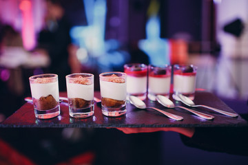Desserts in glasses on a black tray at a party.