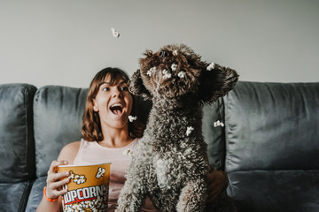 Young girl having a fun afternoon with her nice brown spanish water dog. Sitting on the sofa eating popcorn and having fun. Lifestyle.