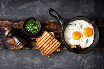 breakfast or brunch fried eggs in black skillet and crispy toasts top view with space for a text