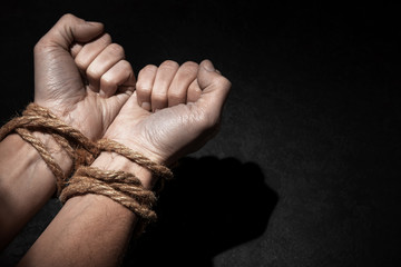 Man with hands tied with rope on black background. The concept of slavery or prisoner. Copy space for text.