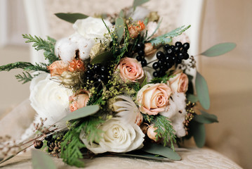 Winter bride's bouquet in pastel colors with roses, spruce, cotton, black berries, feathers and dried flowers rustic. Selective focus